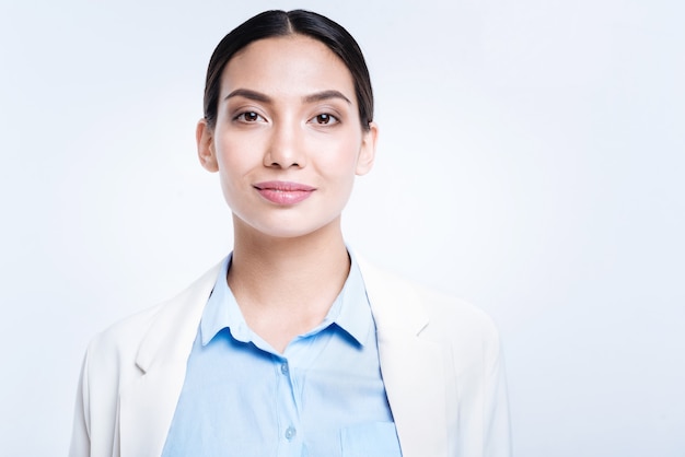 Pleasant doctor. The portrait of a pretty young woman in a medical uniform smiling  while standing isolated on a white wall