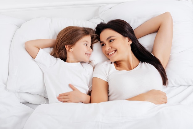 Pleasant girl looking at positive woman while putting her hand behind head and feeling excited