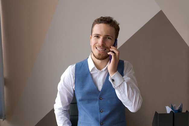 Pleasant handsome bearded man in shirt and waistcoat talking on phone ordering