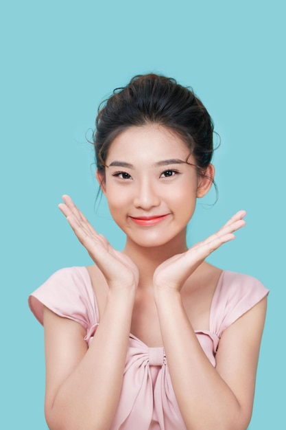 Pleasant looking Asian female model smiles gladfully spreads palms near face expresses positive emotions isolated on cyan background