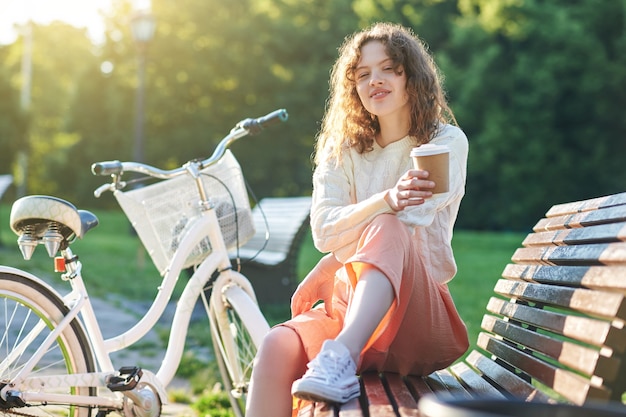 Pleasant moments. Pretty young girl having coffee in the park in the morning