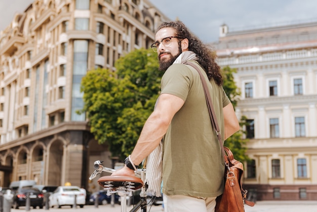 Pleasant nice man looking at the street while standing near his bicycle