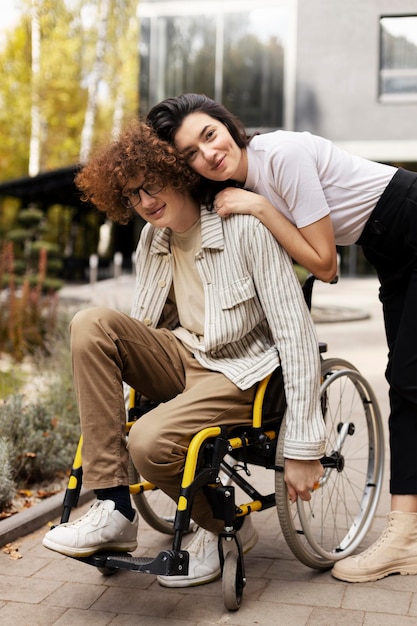 Pleasant positive friends outdoors A young man in a wheelchair his girlfriend hugs him against the background of a building