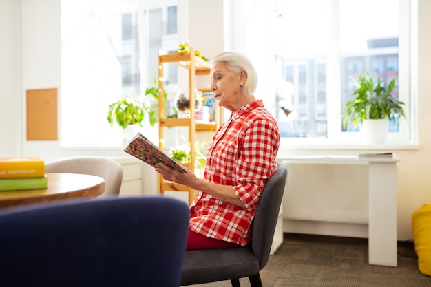 Photo pleasant relaxation. nice aged woman sitting at the table while reading a book at home