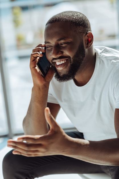 Pleasant talk. Cheerful young smiling afro american man expressing gladness and talking on his smart phone