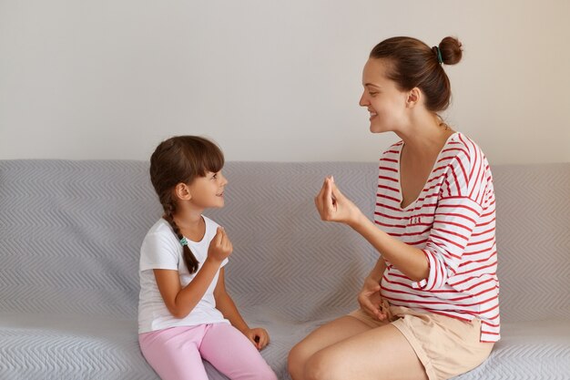 Photo pleasant young adult speech therapist teaching little female kid right sounds pronunciation, professional physiotherapist working on speech defects or difficulties with small child girl indoors.