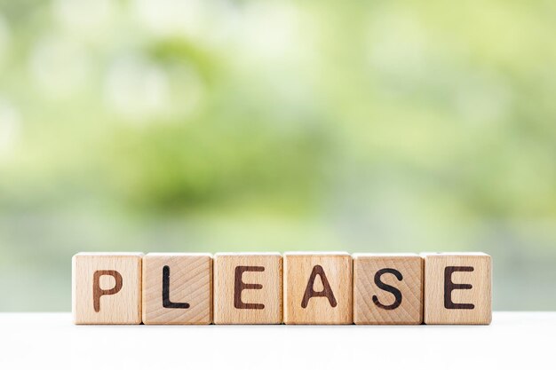 Please word is written on wooden cubes on a green summer background Closeup of wooden elements