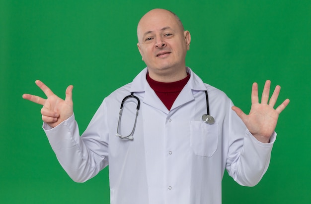 Pleased adult slavic man in doctor uniform with stethoscope gesturing eight with fingers