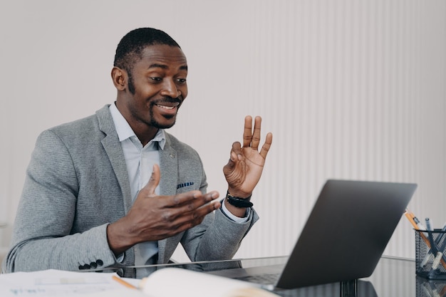 Pleased african american businessman talking by video call at laptop shows ok gesture approves deal