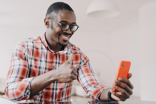 Pleased african american man shows thumb up hand gesture holding phone chatting by video call