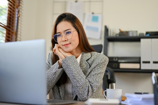 Pleased Asian businesswoman is looking at her laptop screen satisfied with a financial profit