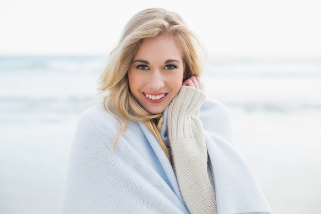 Pleased blonde woman covering herself in a blanket