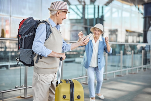 Pleased focused aged male tourist staring at his cellular phone next to a smiling woman