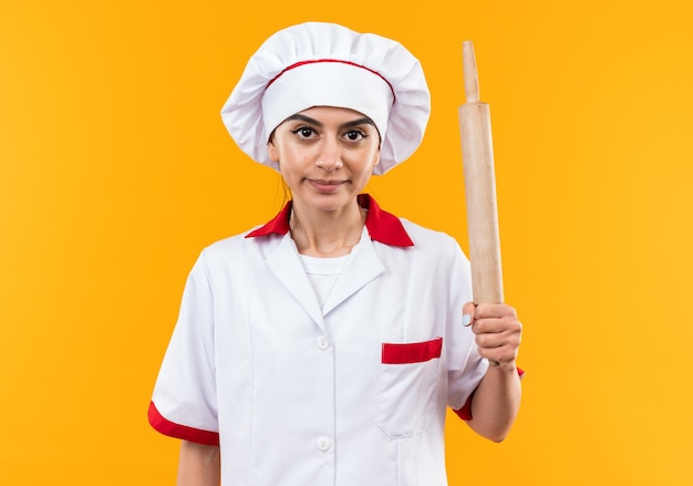 Pleased looking at camera young beautiful girl in chef uniform holding rolling pin 