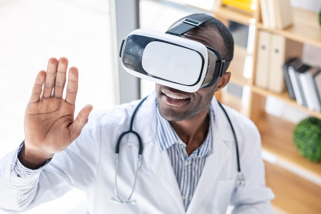 Pleased male person turning head while staring at his hand while using VR mask