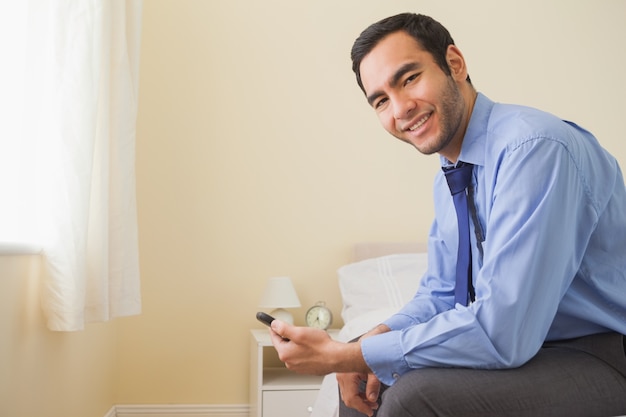 Pleased man looking sitting on bed using a mobile phone