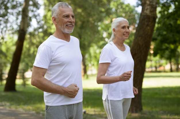 Pleased mature couple keeping their fists clenched while jogging through the park