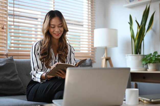 Pleased millennial woman sitting on couch and reading book