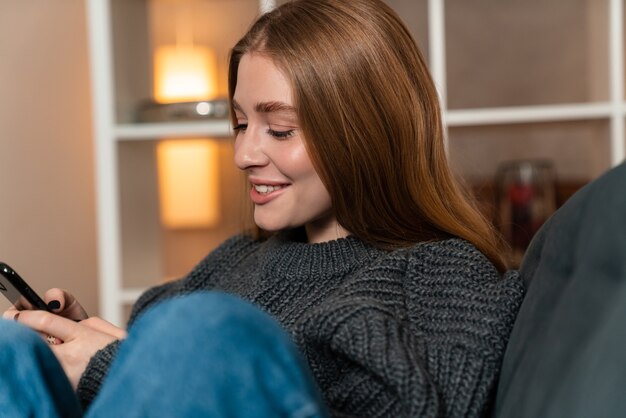 a pleased optimistic cheery young woman indoors at home using mobile phone.