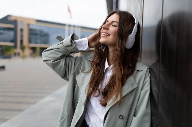 Pleased with herself cheerful stylish girl listens to music in headphones leaning her back against