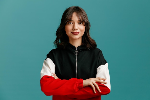 Pleased young caucasian woman looking at camera while keeping arms crossed isolated on blue background