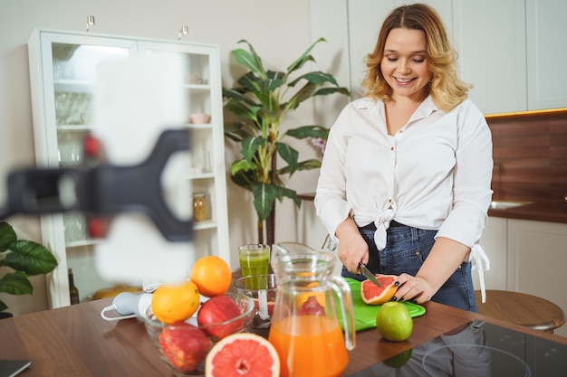 Photo pleased young woman keeping smile on her face while spending her morning in the kitchen