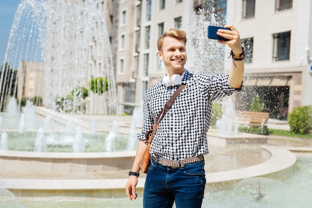 Pleasurable mood. Happy handsome man holding his smartphone while taking a selfie