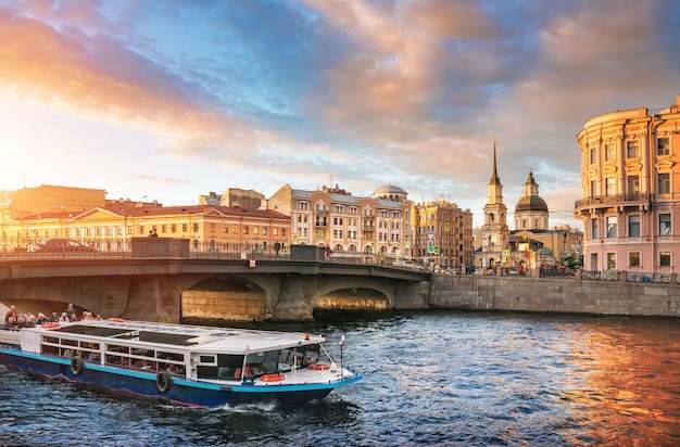 A pleasure boat with tourists at the Belinsky bridge across the Fontanka River in St. Petersburg on a sunny summer evening