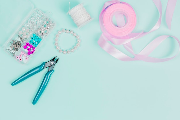 Pliers; pearls; thread spool and pink ribbon on teal background