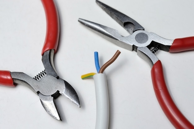 Pliers and stripped three-core wire on a white background close-up.