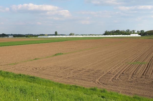 Plowed field furrows left after the passage of the tractor Agriculture providing the population with food and obtaining raw materials for industry Spring agricultural work Greenhouses