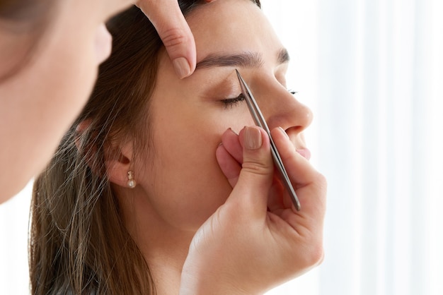 Plucking female eyebrows with tweezers during eyebrow correction in beauty salon