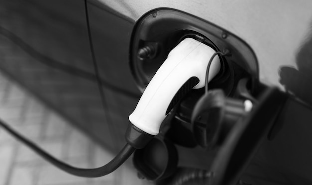 Plugin hybrid EV car charging at charge station home Black and white photo Closeup view