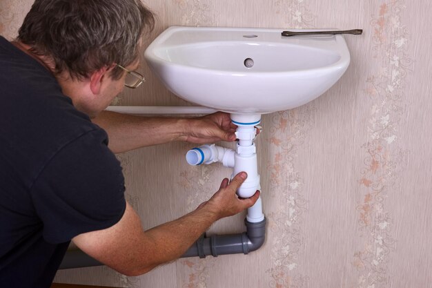 Photo plumber fixes leak in drain pipe by replacing siphon