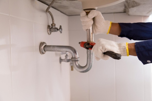 Photo plumber fixing white sink pipe with adjustable wrench