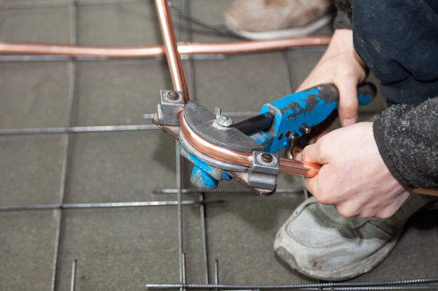 Plumber hands bends copper pipes by pipe bender