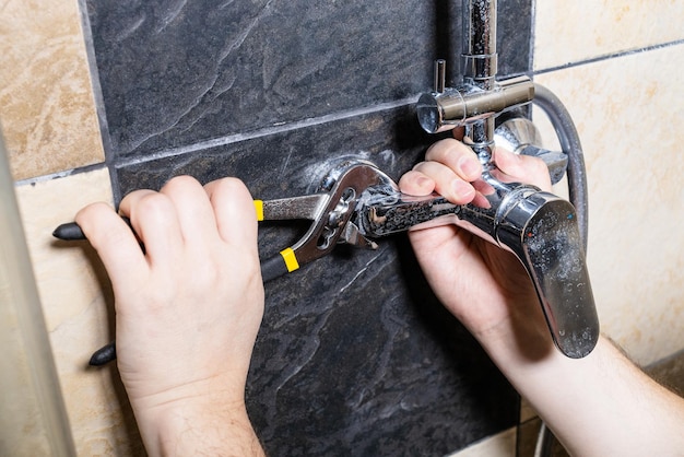 Plumber unscrews shower faucet on tiled wall