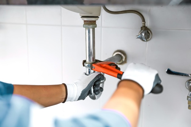 Photo plumber using a wrench to repair a water pipe under the sink