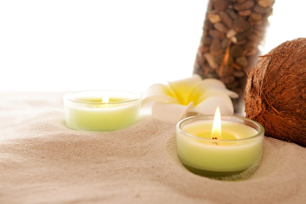 Plumeria with burning candles coconut and bottle on sand isolated on white