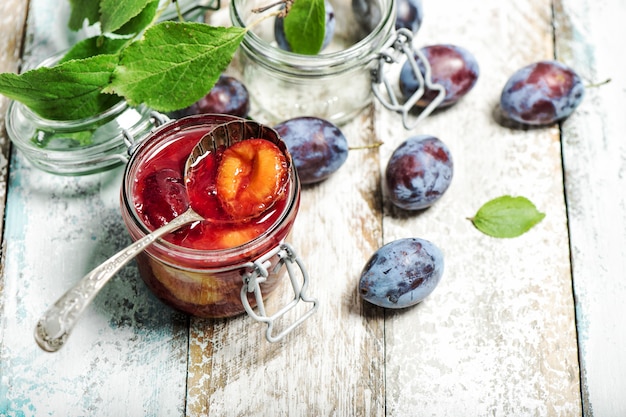 Plums jam with fresh fruits on wooden background. Marmalade preparing