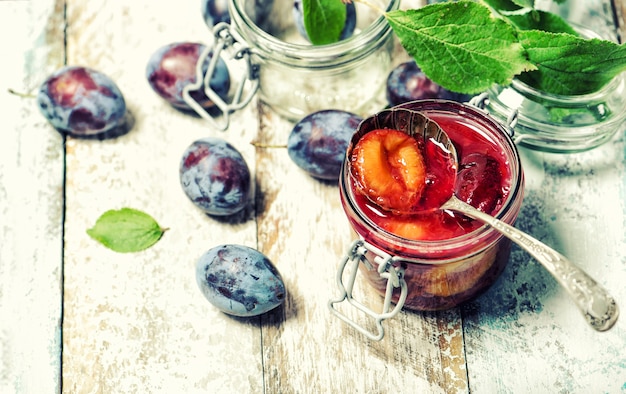 Plums jam with fresh fruits on wooden background. Vintage style toned picture