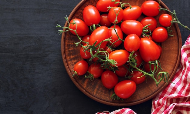 Plumshaped cherry tomatoes on a clay bowl on a black wooden background top view