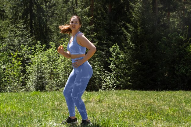 Plus size girl doing physical exercise sports and running in a blue tight suit outdoors