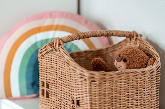 A plush toy bear sits in a wicker basket in the form of a house, a childhood concept