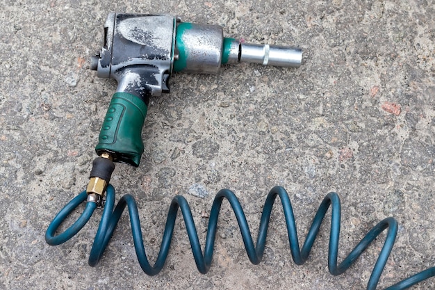 Pneumatic wrench with a green hose lying on the stone paved floor closeup top view