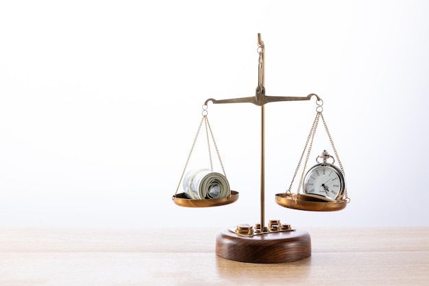 Pocket clock and some money scaling equally on a scale on a wooden surface