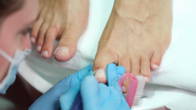 Podiatrist making professional pedicure of toe nails in beauty salon closeup