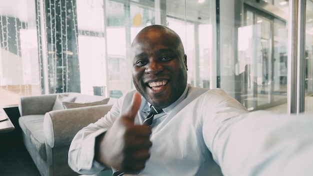 Point of view shot of businessman in formal wear having online video chat with family on smartphone and waving his hand happily in a classy cafe He smiles cheerfully