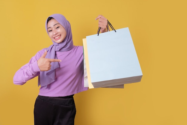 Pointing of beautiful asian woman showing shopping bags, wearing purple T shirt