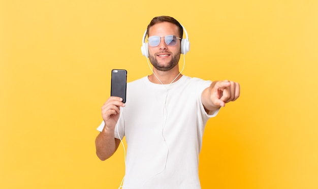 Pointing at camera choosing you, listening music with headphones and a smartphone